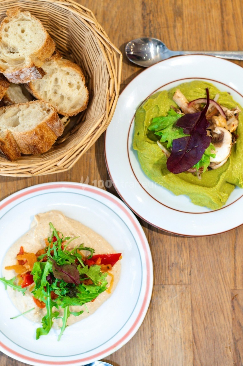 Assiette de houmous garni, crêpe verte aux légumes et corbeille de pain sur une table en bois.
