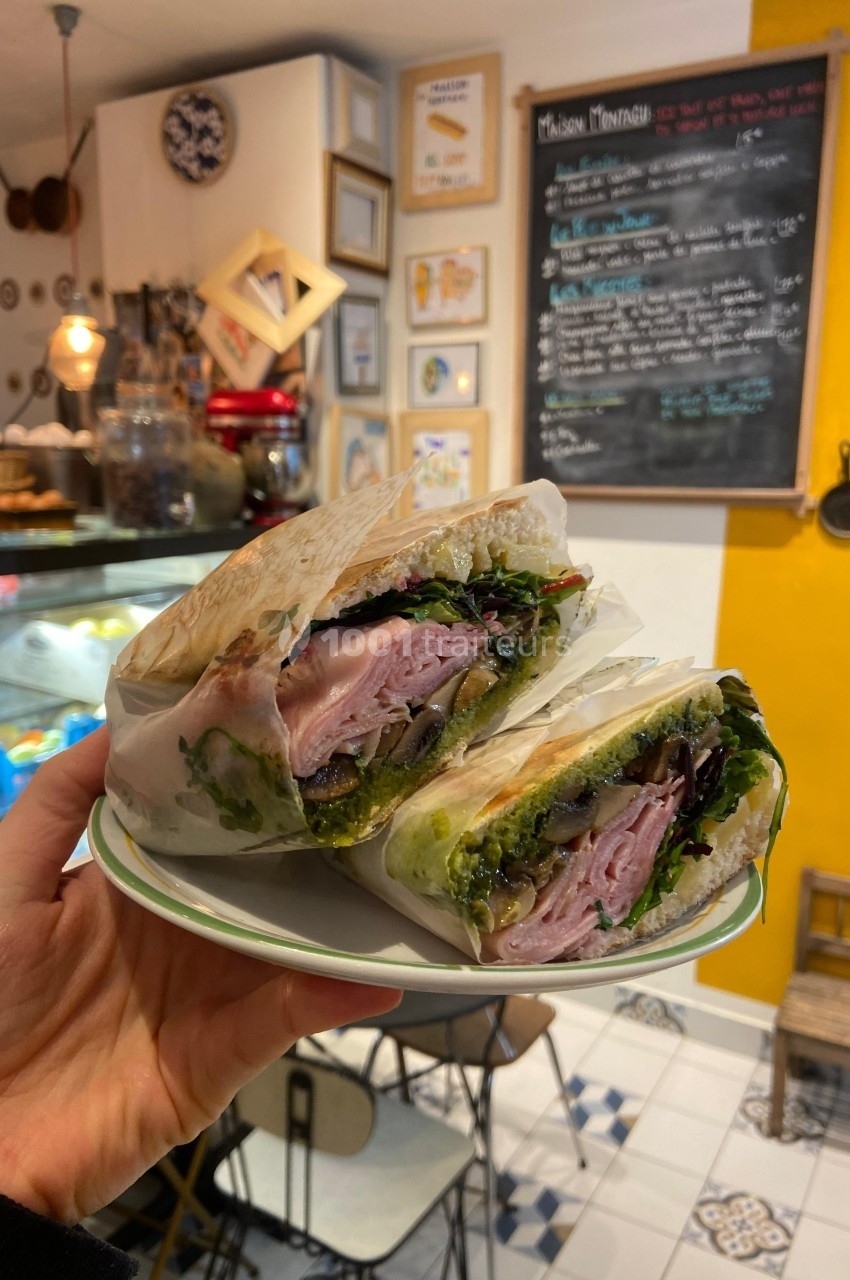 Sandwich garni de jambon, légumes frais et sauce, présenté sur une assiette dans un café au décor chaleureux.