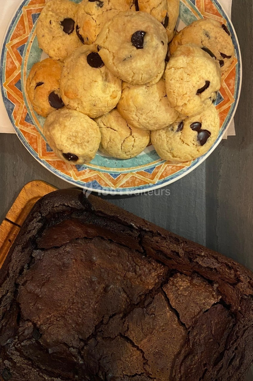 Assiette de cookies aux pépites de chocolat et plat de brownie posé sur une table sombre.
