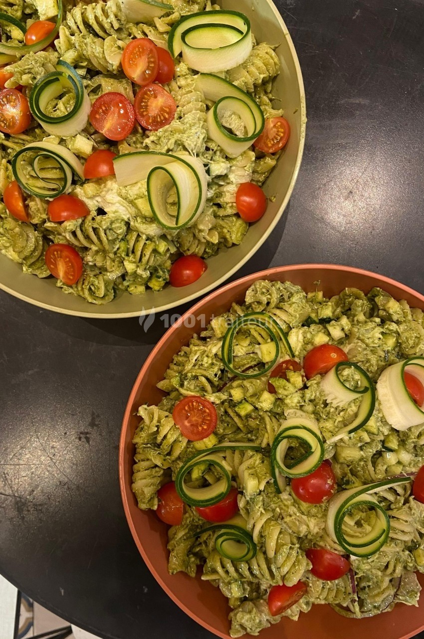 Deux assiettes de pâtes au pesto garnies de tomates cerises et de rubans de courgettes sur une table noire.