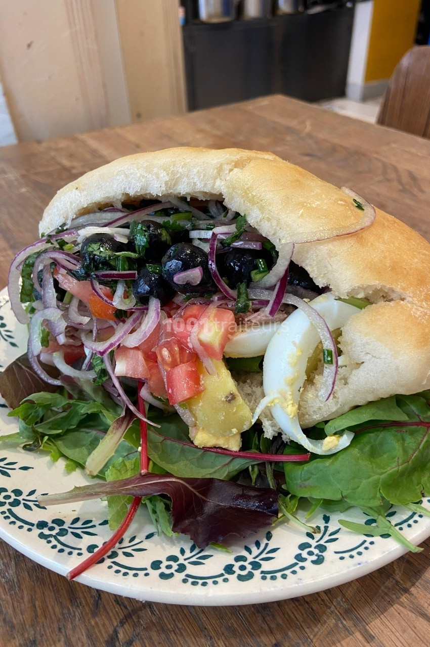 Sandwich pita garni de légumes frais, œufs durs, olives et avocat, servi sur une assiette avec des feuilles de salade.