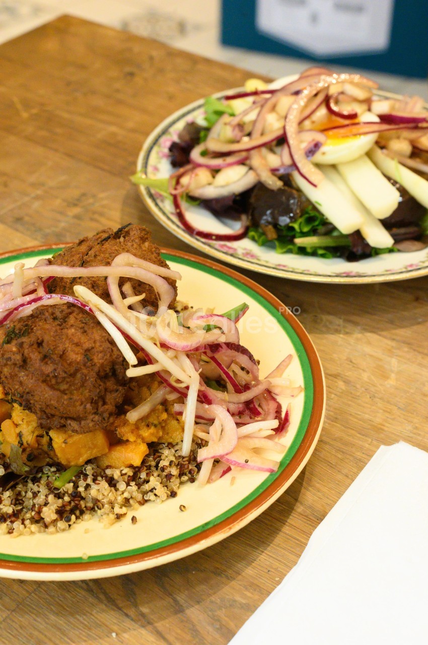 Assiette de quinoa avec boulettes végétariennes, oignons rouges et légumes, accompagnée d'une salade verte et œufs durs.
