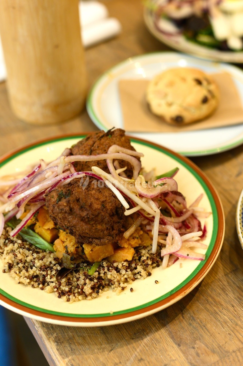 Assiette de quinoa garnie de falafels, légumes rôtis et salade d'oignons rouges, avec un cookie en arrière-plan.