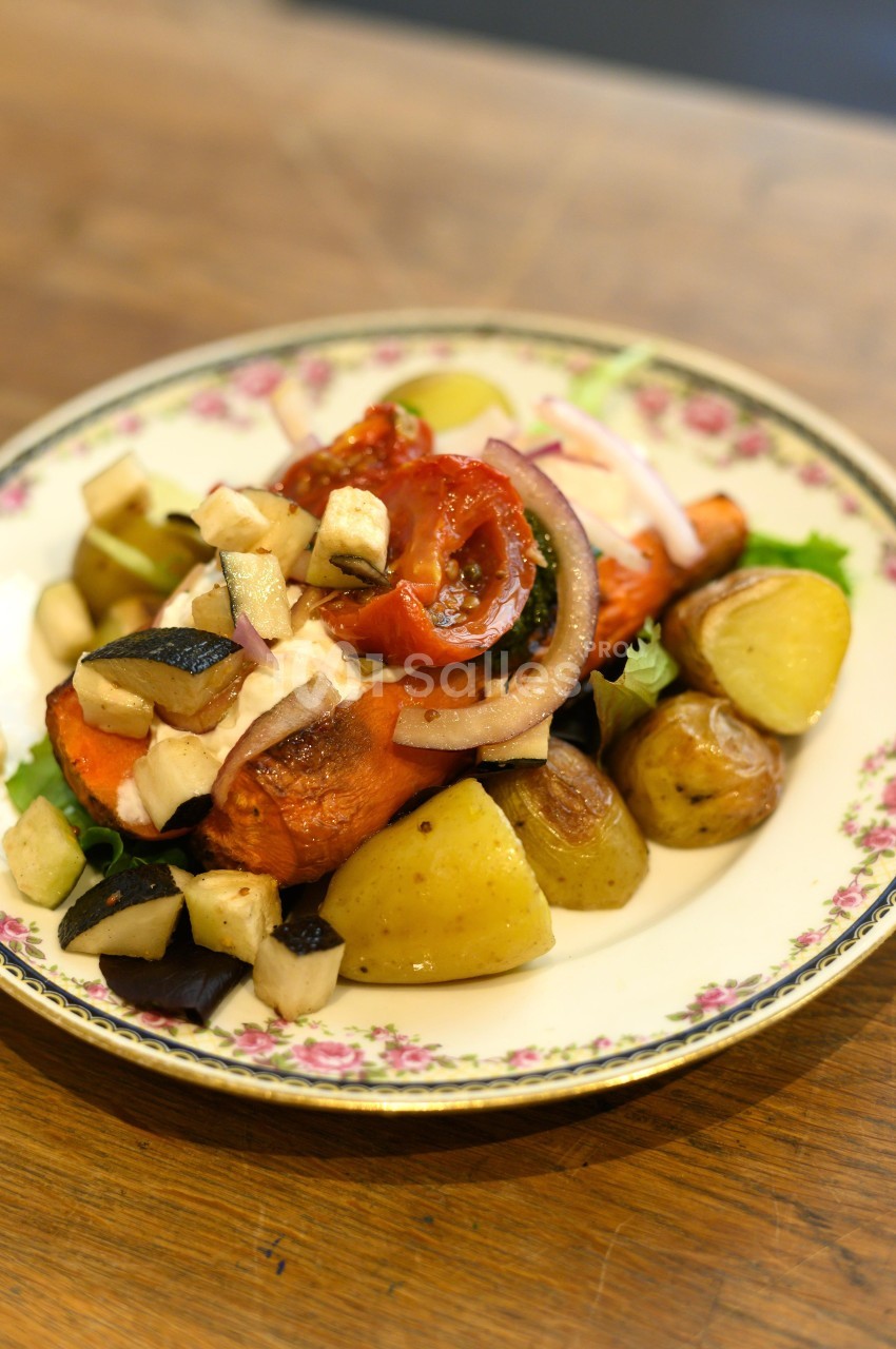 Assiette de légumes rôtis comprenant pommes de terre, carottes, aubergines, tomates et oignons, servie sur un plat décoré.