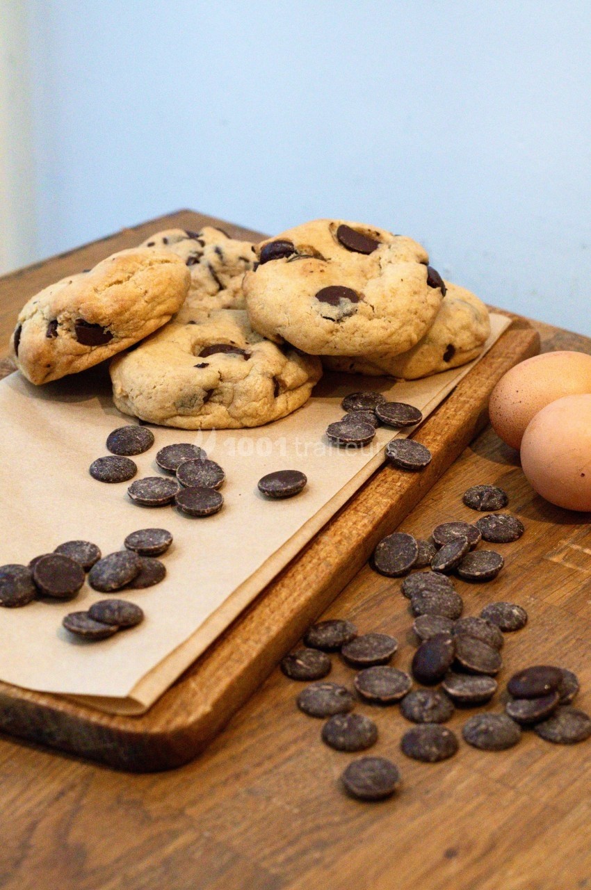 Cookies aux pépites de chocolat sur une planche en bois, entourés de pépites de chocolat et d'œufs.
