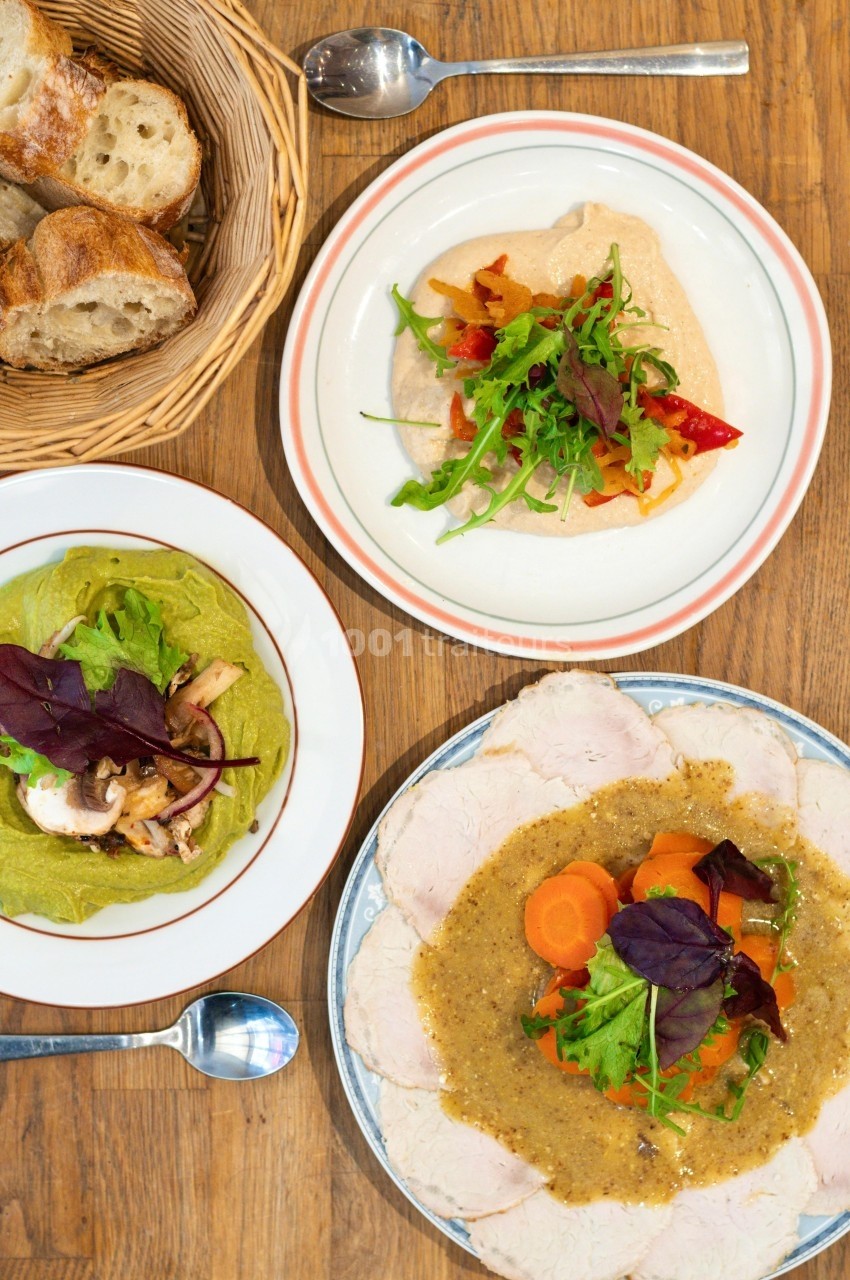 Assiette de viande avec sauce et légumes, houmous garni, salade verte, et pain dans un panier sur une table en bois.