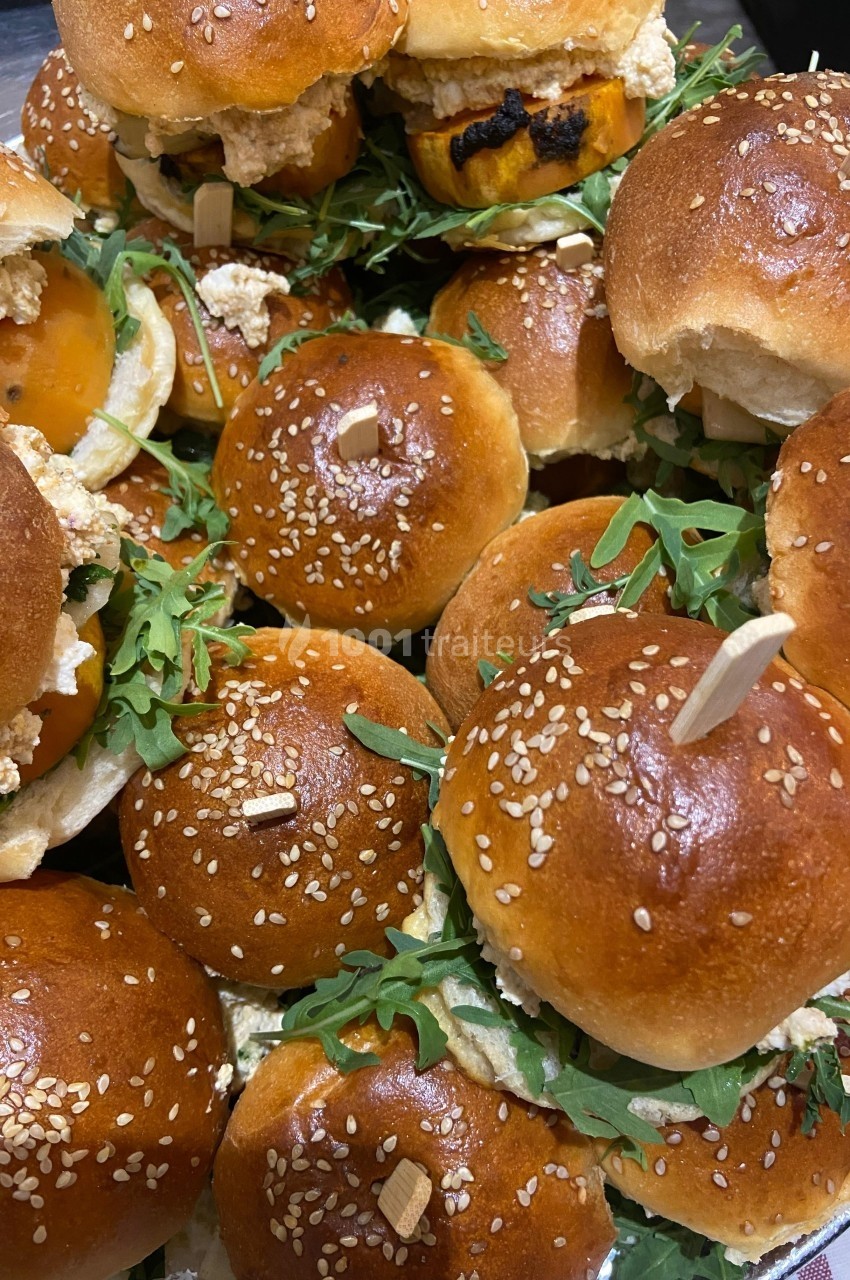 Plateau de mini-burgers garnis de roquette, fromage et autres ingrédients, avec pains briochés aux graines de sésame.