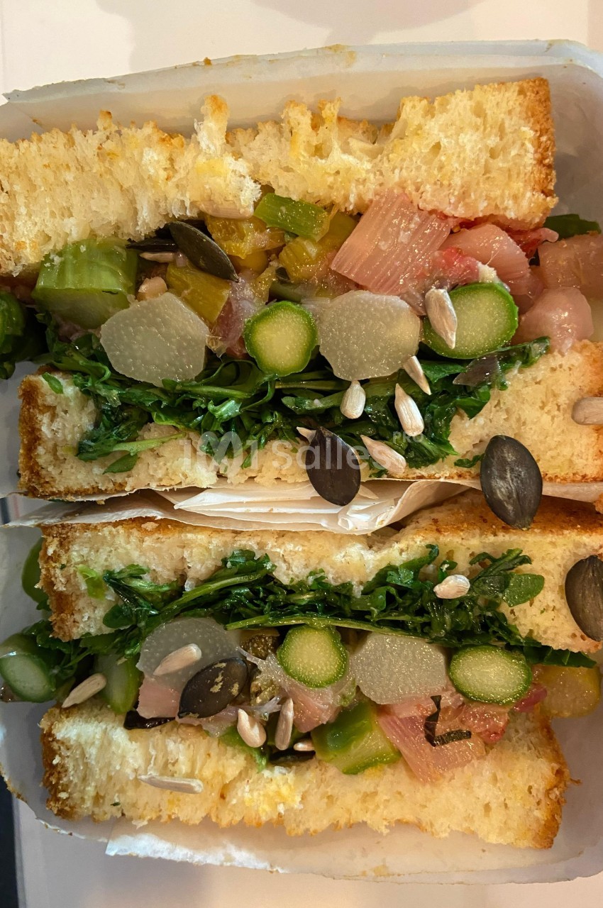 Sandwich garni de légumes frais, graines, asperges et verdure, présenté en coupe sur du pain moelleux.