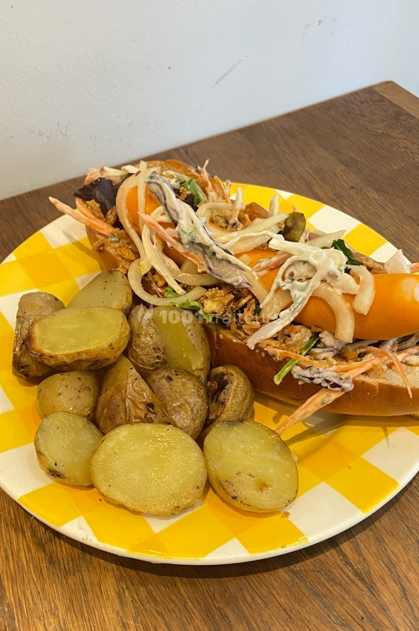 Assiette contenant un sandwich garni de légumes et une portion de pommes de terre rôties sur une table en bois.