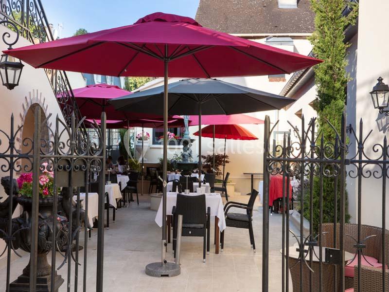 Terrasse extérieure d'un restaurant avec tables dressées, chaises noires et parasols colorés sous un ciel dégagé.