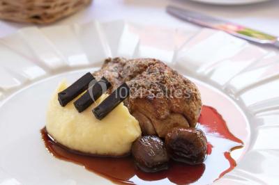 Dessert au glaçage chocolat brillant, garni de noisettes entières et concassées, présenté sur une assiette blanche.