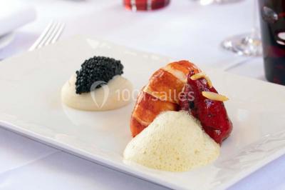 Dessert au glaçage chocolat brillant, garni de noisettes entières et concassées, présenté sur une assiette blanche.