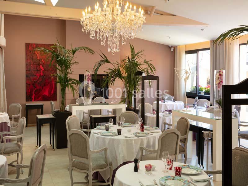 Salle de restaurant élégante avec tables dressées, chaises classiques, lustre en cristal et décorations végétales.
