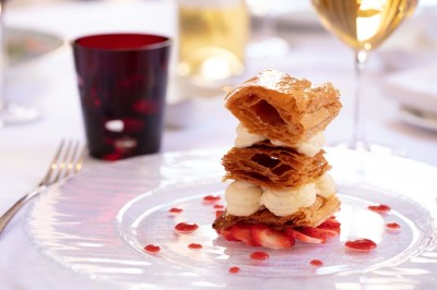 Dessert au glaçage chocolat brillant, garni de noisettes entières et concassées, présenté sur une assiette blanche.