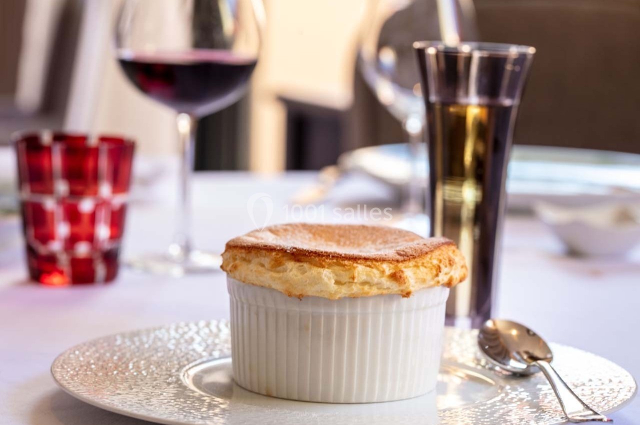 Soufflé doré servi dans un ramequin blanc sur une table dressée avec des verres de vin et d'eau.