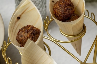 Boules de falafel servies dans des cônes en bois, présentées sur un présentoir doré avec des décorations florales en arrière…