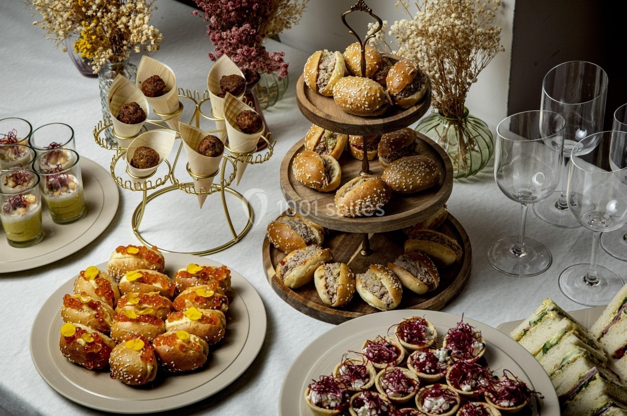 Buffet avec mini-sandwichs, verrines, canapés variés et décorations florales sur une table blanche.