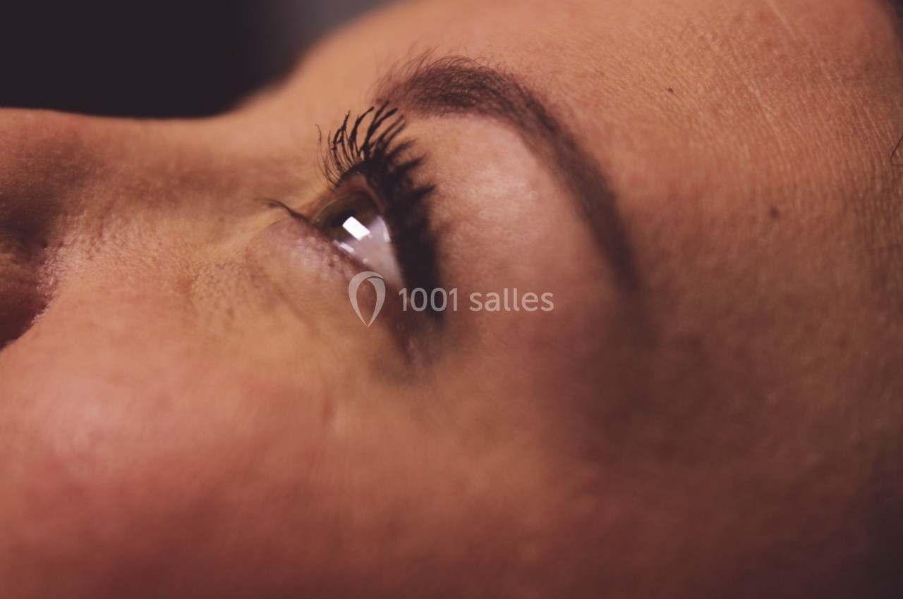 Gros plan sur le visage d'une femme, mettant en valeur son œil ouvert et ses cils sous un éclairage doux.