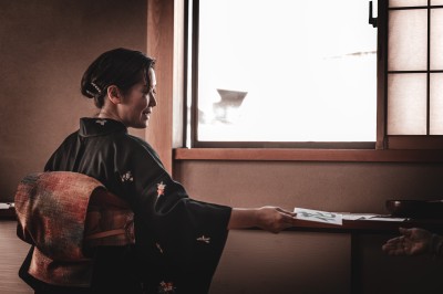 Femme assise dans une lumière tamisée, entourée de verres, regardant vers l'objectif.