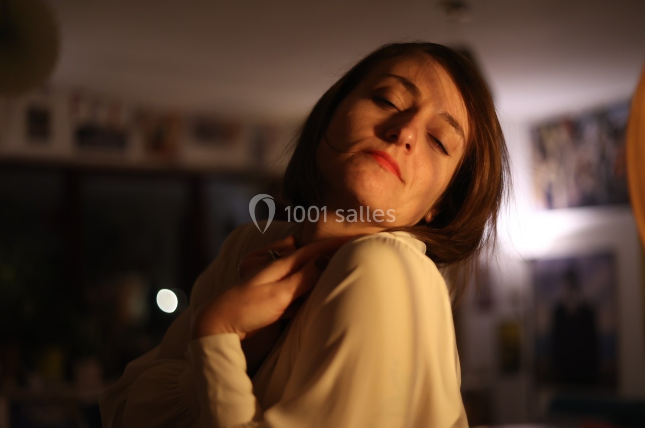 Femme aux yeux fermés, tête légèrement inclinée, éclairée par une lumière chaude dans un intérieur sombre.