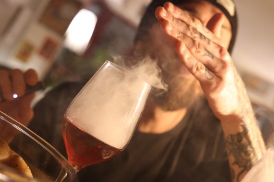 Femme assise dans une lumière tamisée, entourée de verres, regardant vers l'objectif.