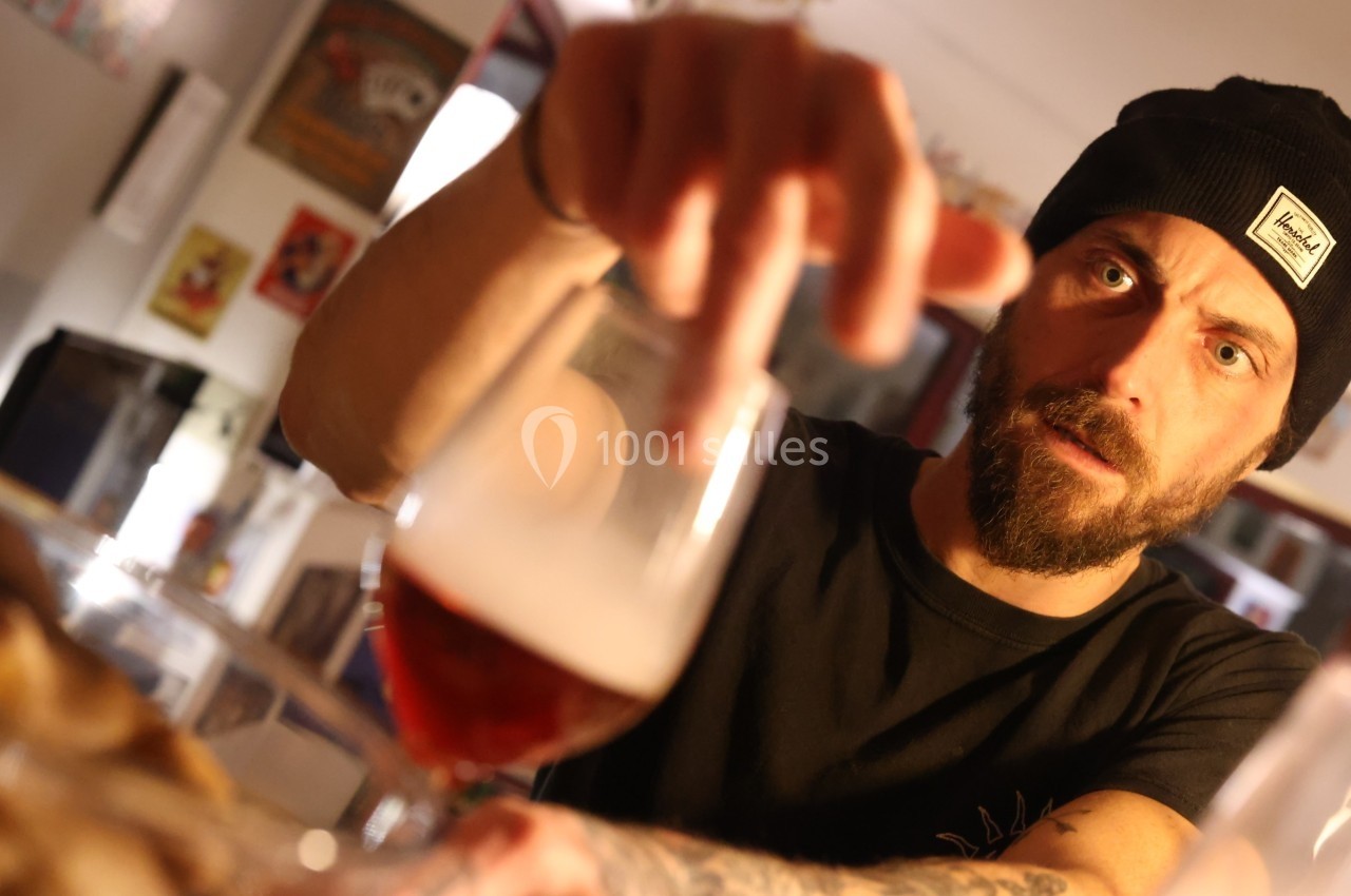 Un homme portant un bonnet tend la main vers un verre de bière dans un intérieur chaleureux.