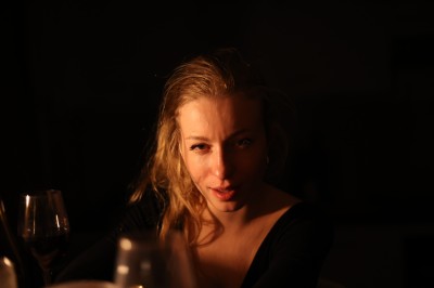 Femme assise dans une lumière tamisée, entourée de verres, regardant vers l'objectif.