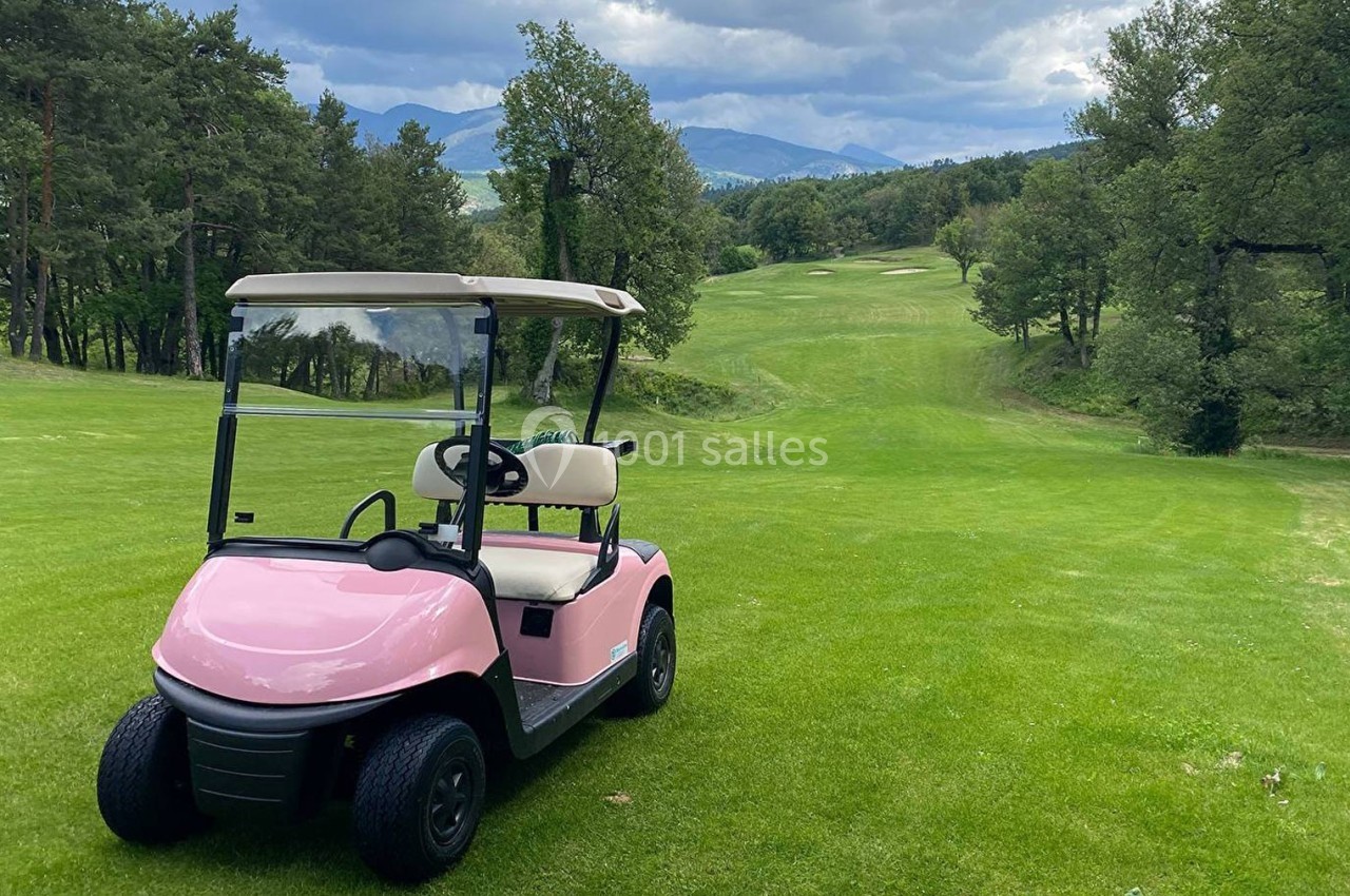 Voiturette de golf rose stationnée sur un terrain verdoyant entouré d'arbres, avec des collines en arrière-plan.