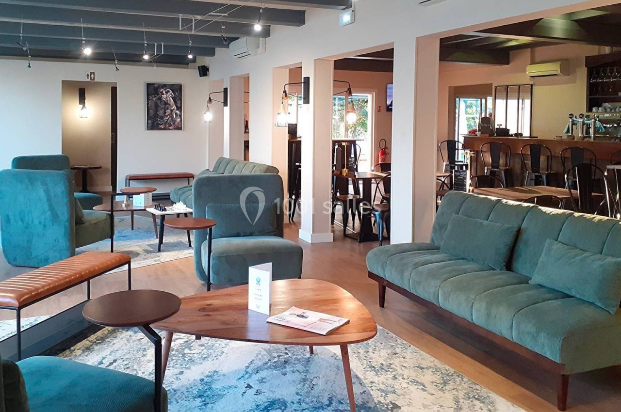 Espace intérieur lumineux avec canapés verts, tables en bois et bar en arrière-plan dans un cadre moderne et chaleureux.