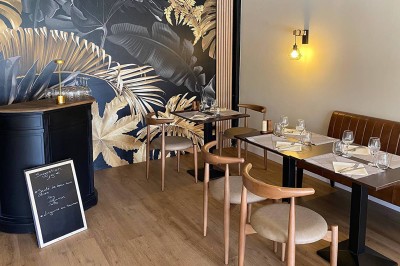 Chambre lumineuse avec lit double, télévision murale, bureau en bois, deux chaises et rideaux blancs filtrant la lumière.