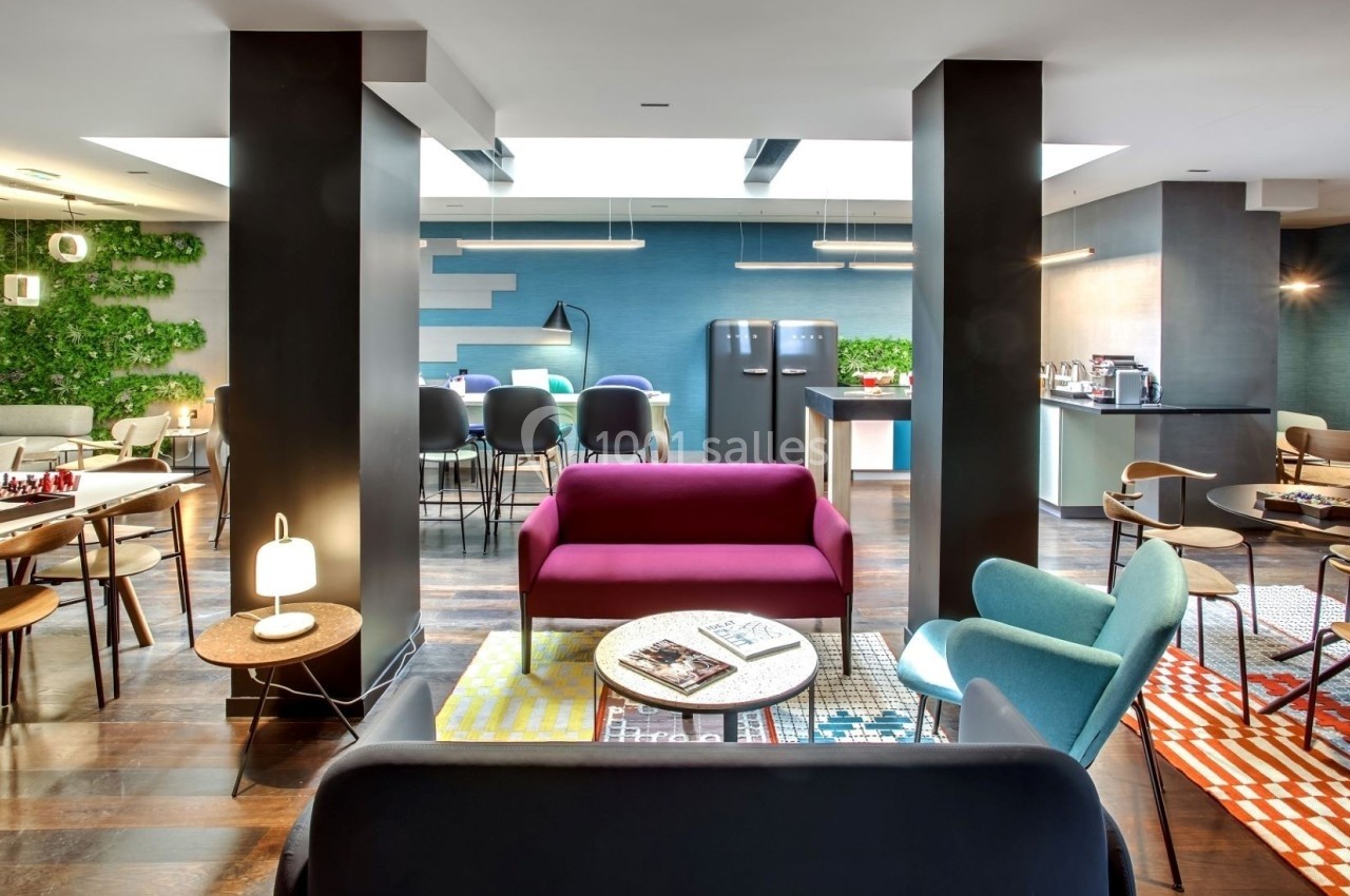 Espace intérieur moderne avec mobilier coloré, coin détente, tables, chaises et mur végétal en arrière-plan.