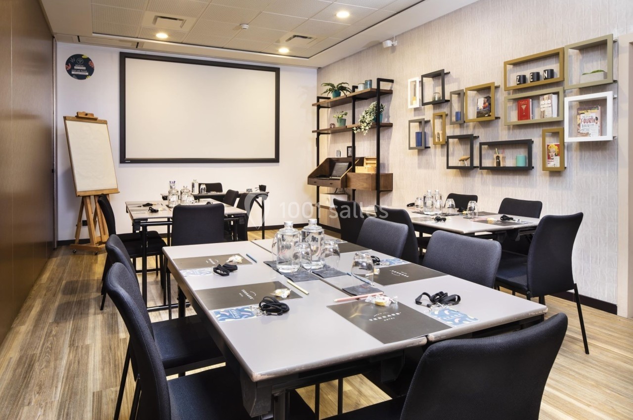 Salle de réunion équipée avec tables, chaises, écran de projection, tableau blanc et étagères décoratives.
