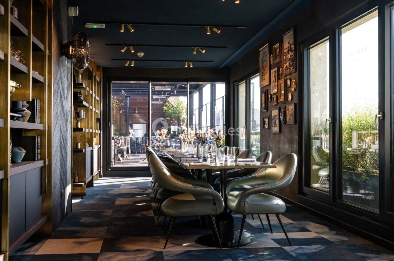 Salle de restaurant moderne avec table dressée, chaises design, étagères décoratives et grandes baies vitrées donnant sur…