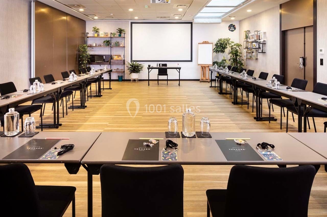 Salle de réunion lumineuse avec tables disposées en U, écran de projection et décorations végétales.