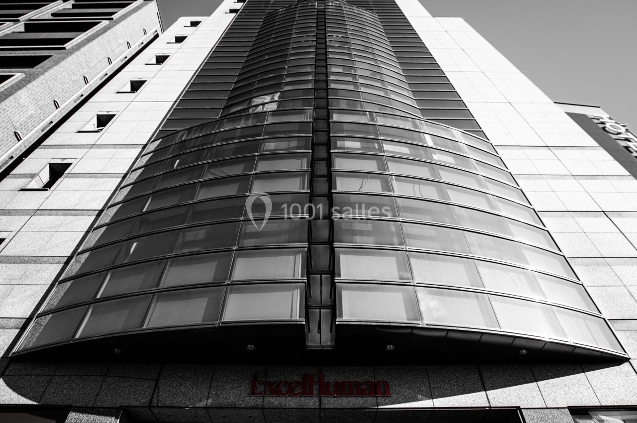 Façade d'un immeuble moderne en verre et métal, vue en contre-plongée, sous un ciel dégagé.