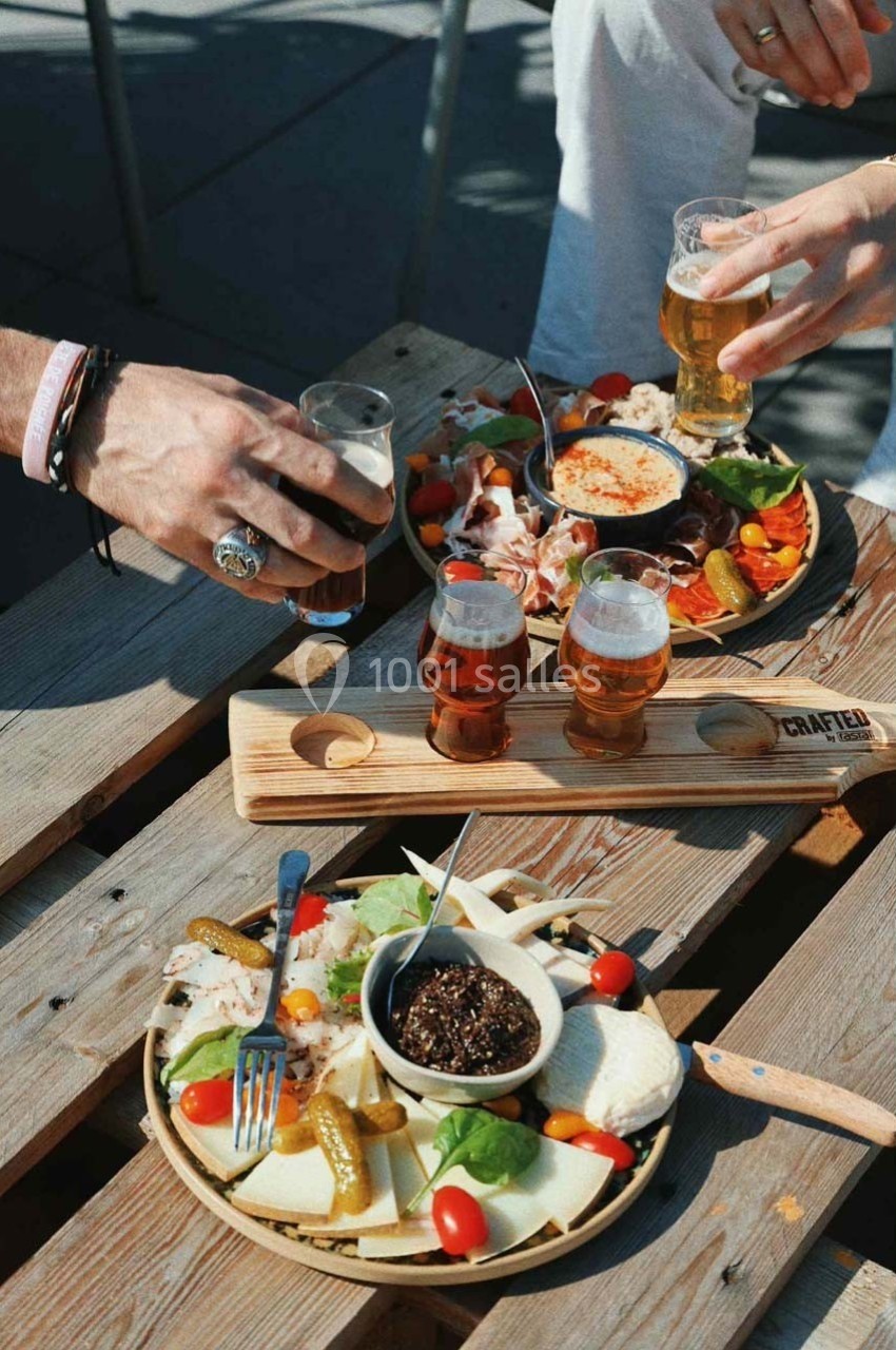 Assiettes de charcuterie et fromage accompagnées de bières artisanales sur une table en bois en extérieur.