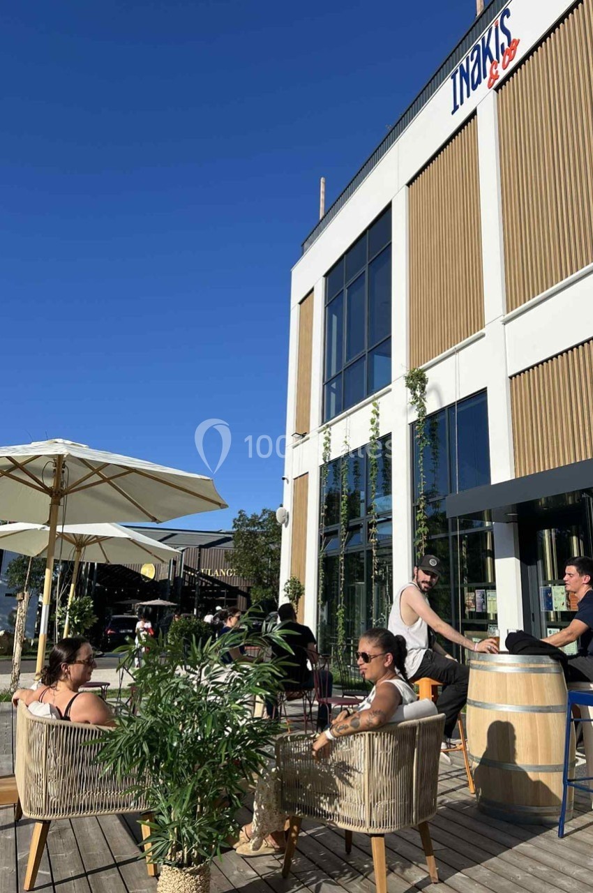 Des personnes assises en terrasse autour de tables, devant un bâtiment moderne avec une enseigne visible.