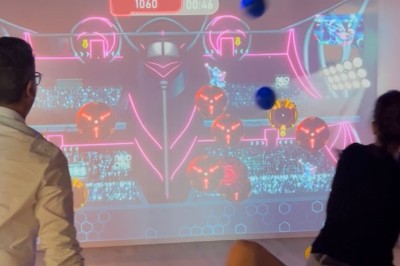 Des personnes jouent à un jeu interactif projeté sur un mur, utilisant des ballons pour toucher des cibles lumineuses.