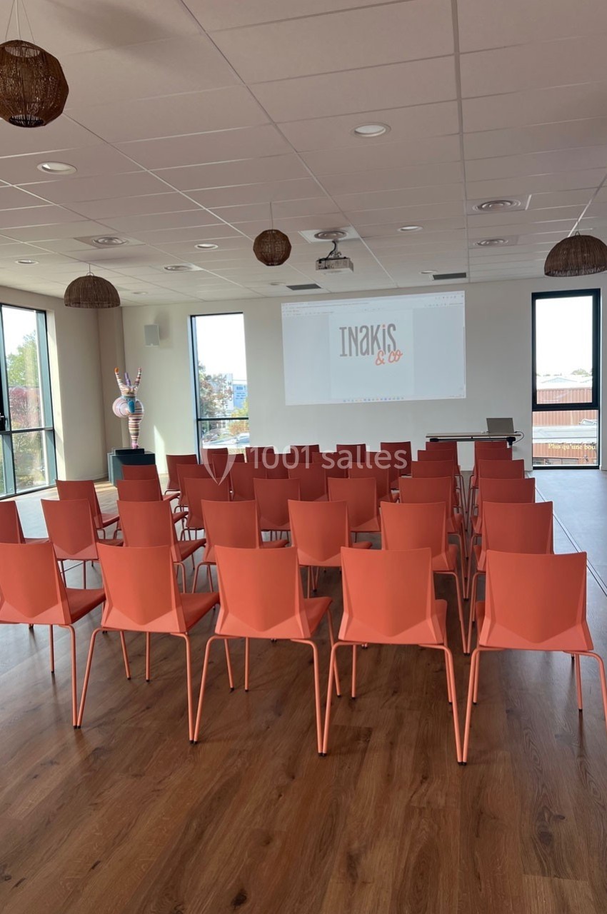 Salle de réunion lumineuse avec des chaises orange alignées face à un écran de projection.