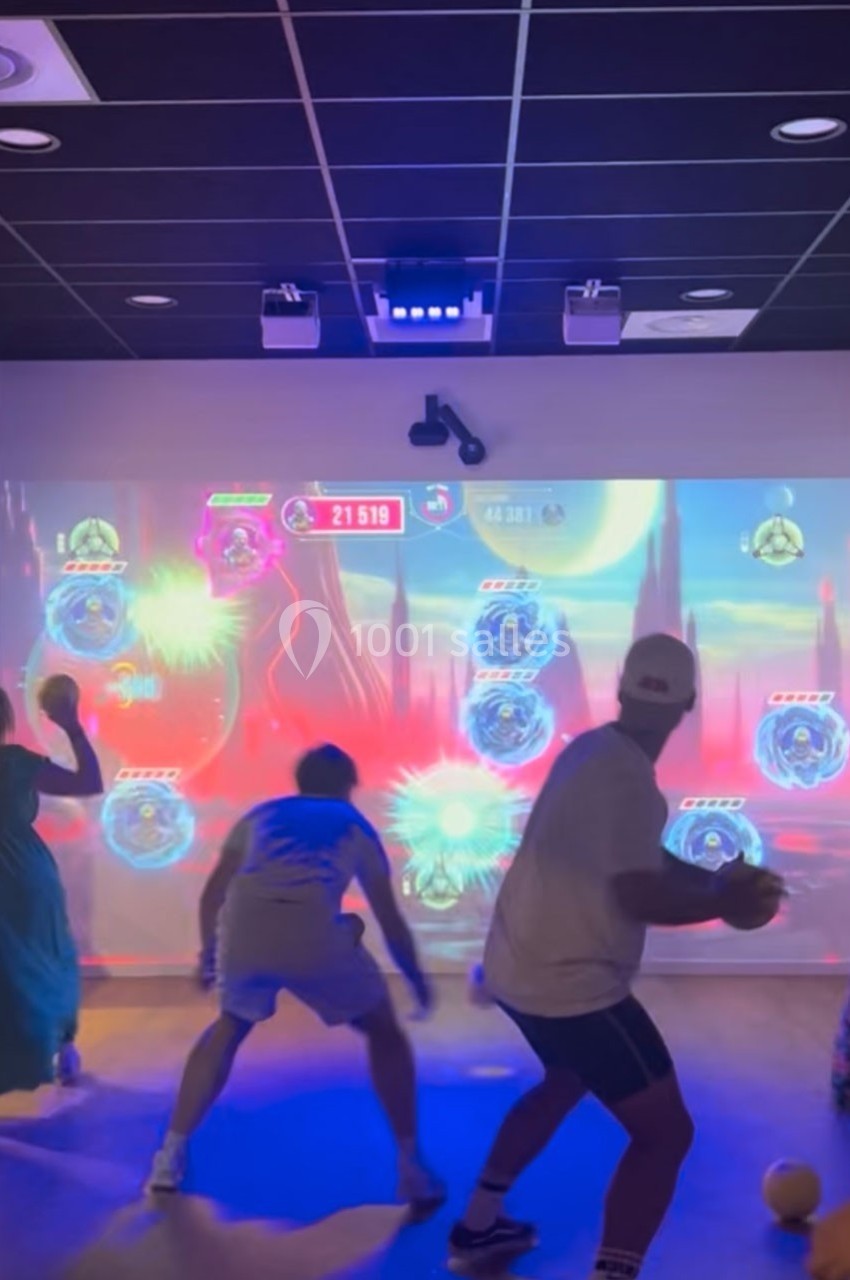 Des personnes jouent à un jeu interactif projeté sur un mur, utilisant des ballons pour toucher des cibles lumineuses.