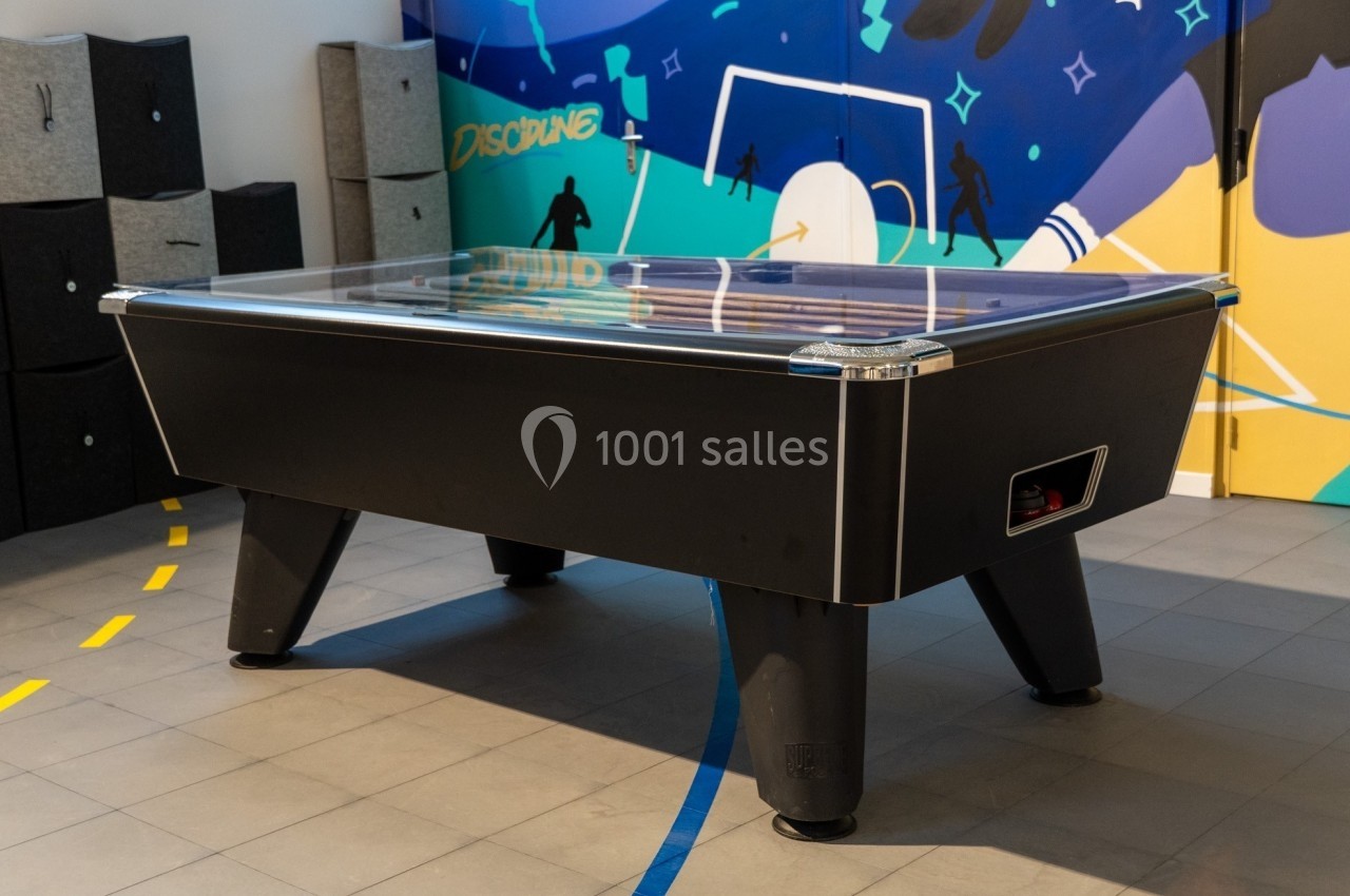 Table de air hockey noire dans une salle de loisirs avec un mur coloré en arrière-plan.