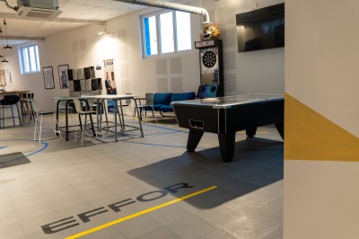 Espace de coworking moderne avec comptoir en bois, chaises hautes et mur décoré de fresques colorées.