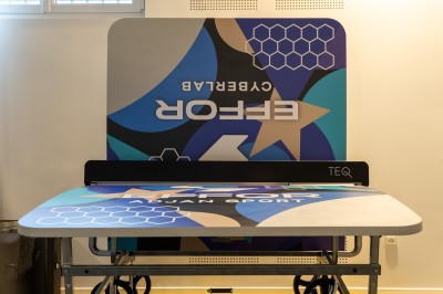 Espace de coworking moderne avec comptoir en bois, chaises hautes et mur décoré de fresques colorées.