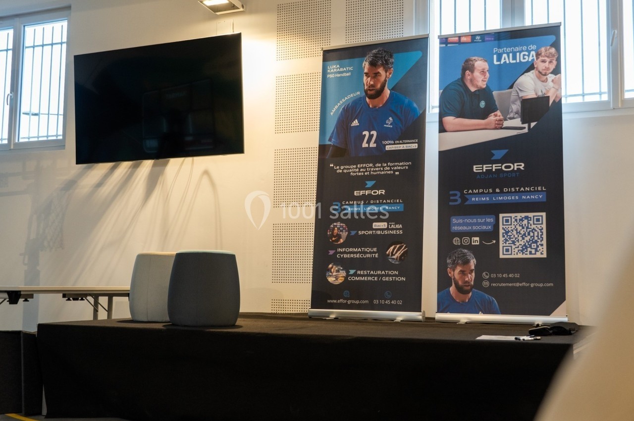 Bannière promotionnelle d'une école avec informations sur ses formations, posée dans une salle équipée d'un écran.