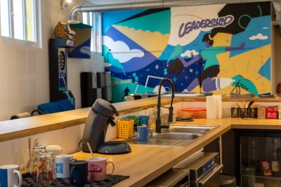 Espace de coworking moderne avec comptoir en bois, chaises hautes et mur décoré de fresques colorées.