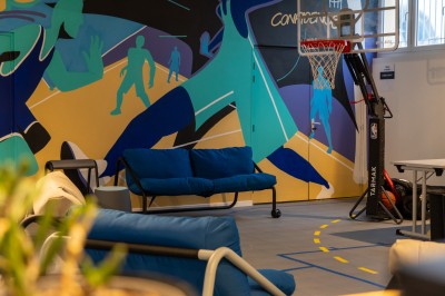 Espace de coworking moderne avec comptoir en bois, chaises hautes et mur décoré de fresques colorées.