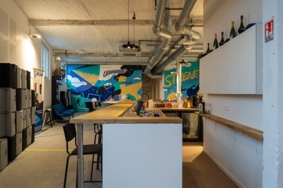 Espace de coworking moderne avec comptoir en bois, chaises hautes et mur décoré de fresques colorées.