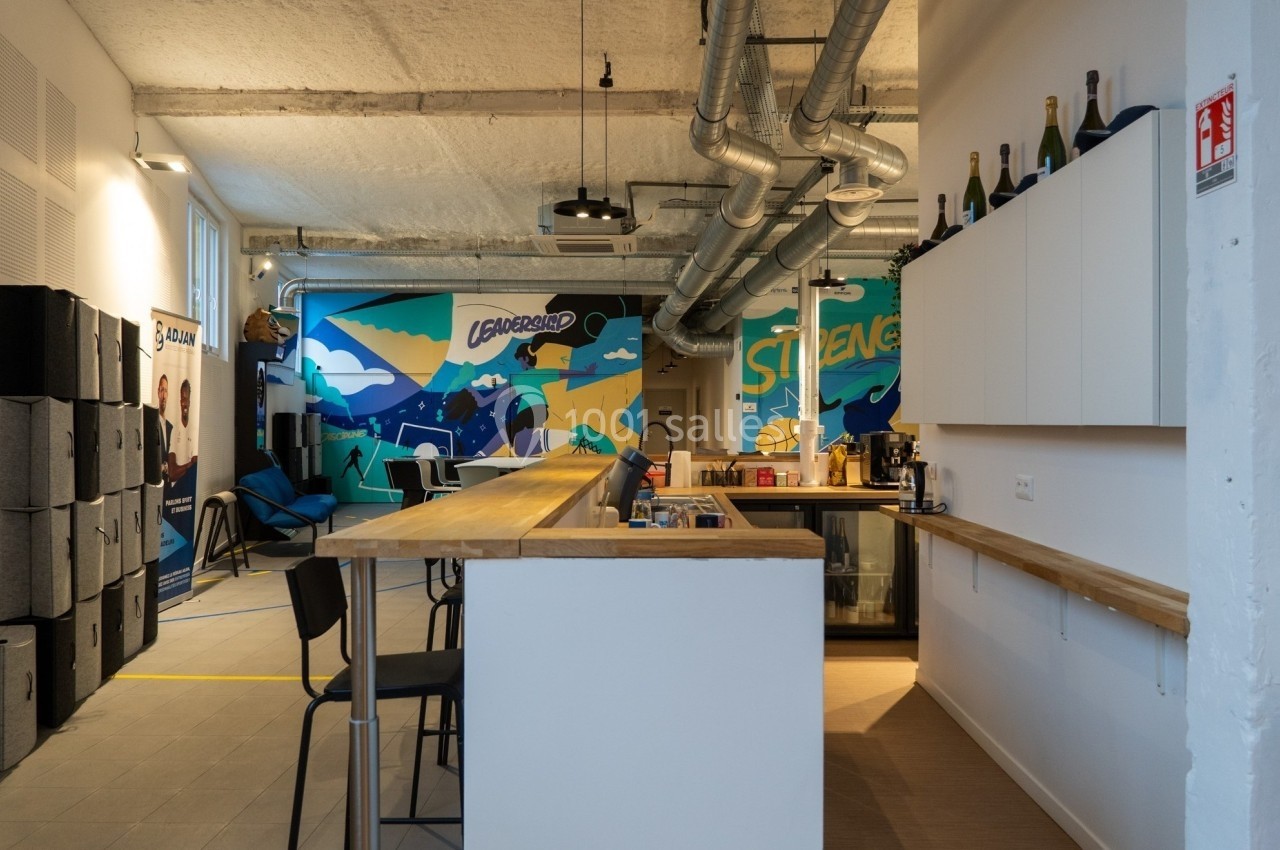 Espace de coworking moderne avec comptoir en bois, chaises hautes et mur décoré de fresques colorées.