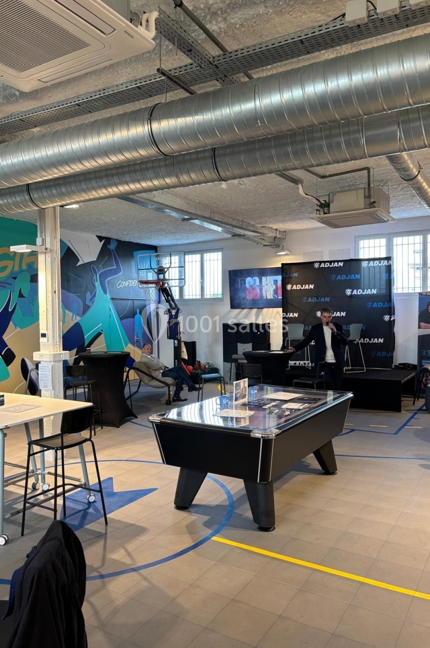 Espace intérieur moderne avec table de billard, fresque murale colorée et présentation en cours devant un stand.