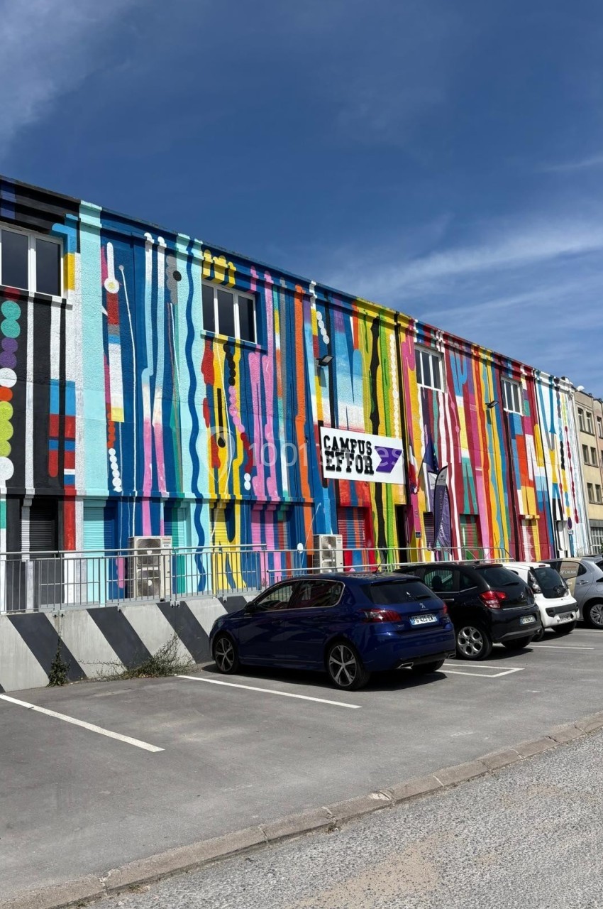 Façade colorée d'un bâtiment avec des motifs abstraits, un panneau ’Campus E2C’ et un parking à l'avant.